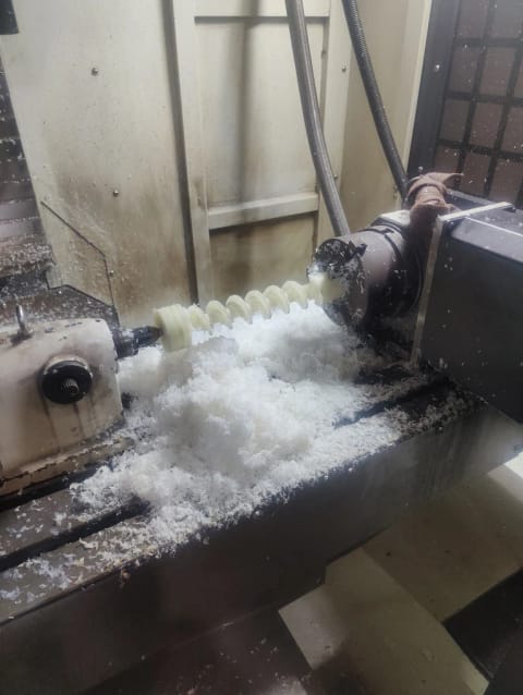 Auger screw being turned on a CNC lathe, with white polymer swarf around the workpiece