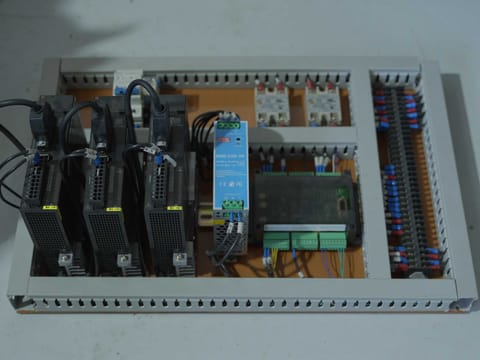 Technician working at an open electrical control cabinet containing servo drives